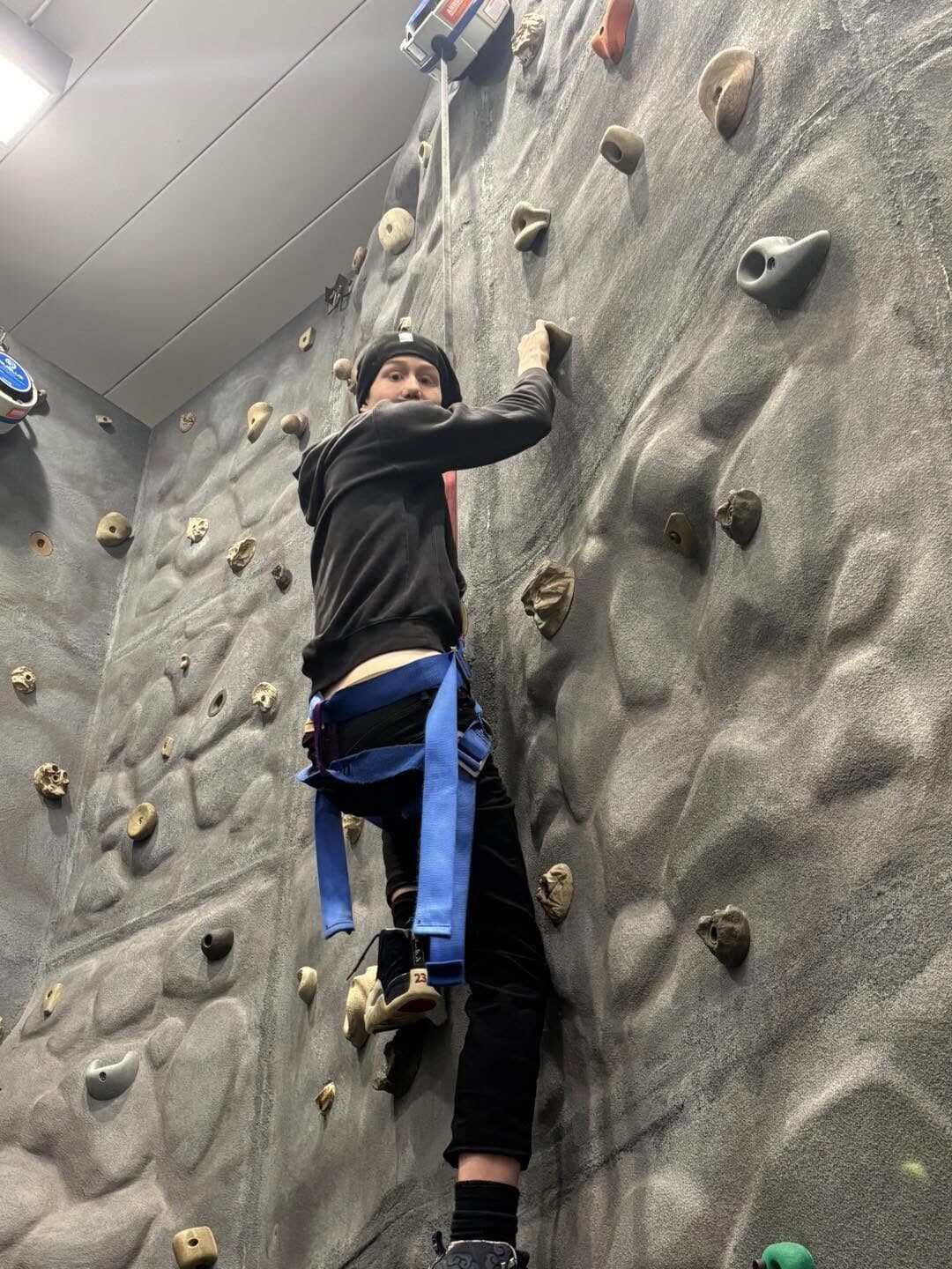 A student climbing near the top of an indoor climbing wall