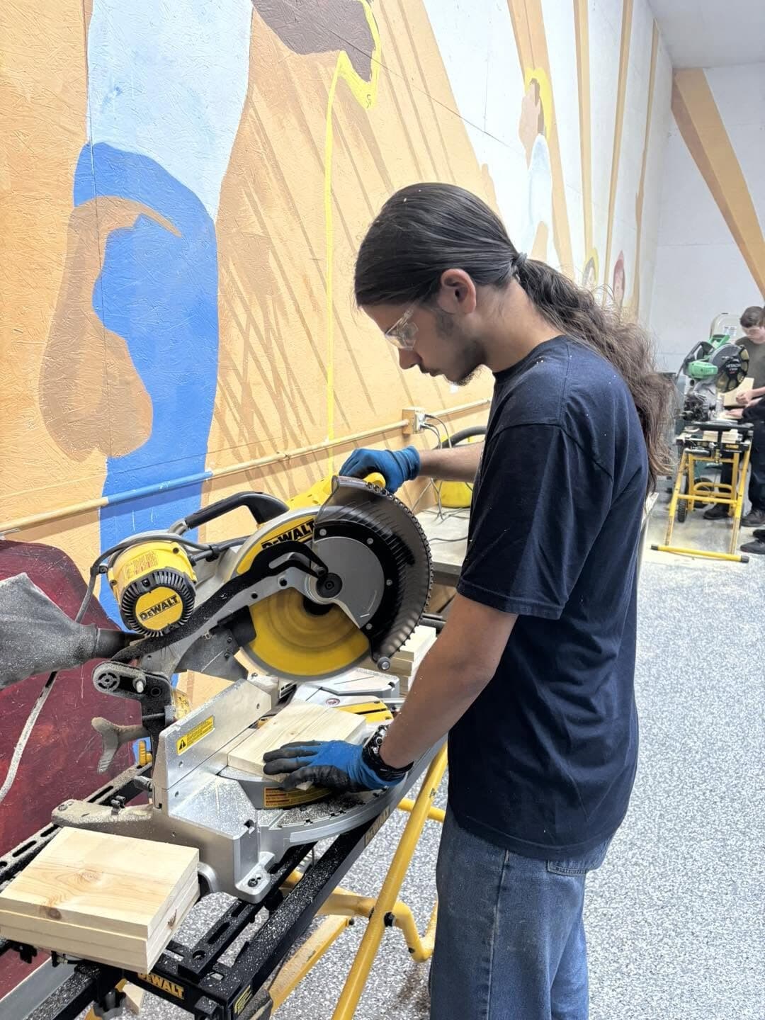 A student cutting wood at a miter saw in the shop